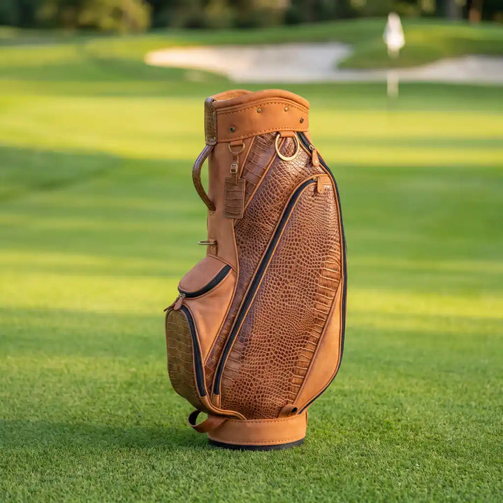 A tan and brown leather golf bag with crocodile-embossed panels, standing on a green golf course.