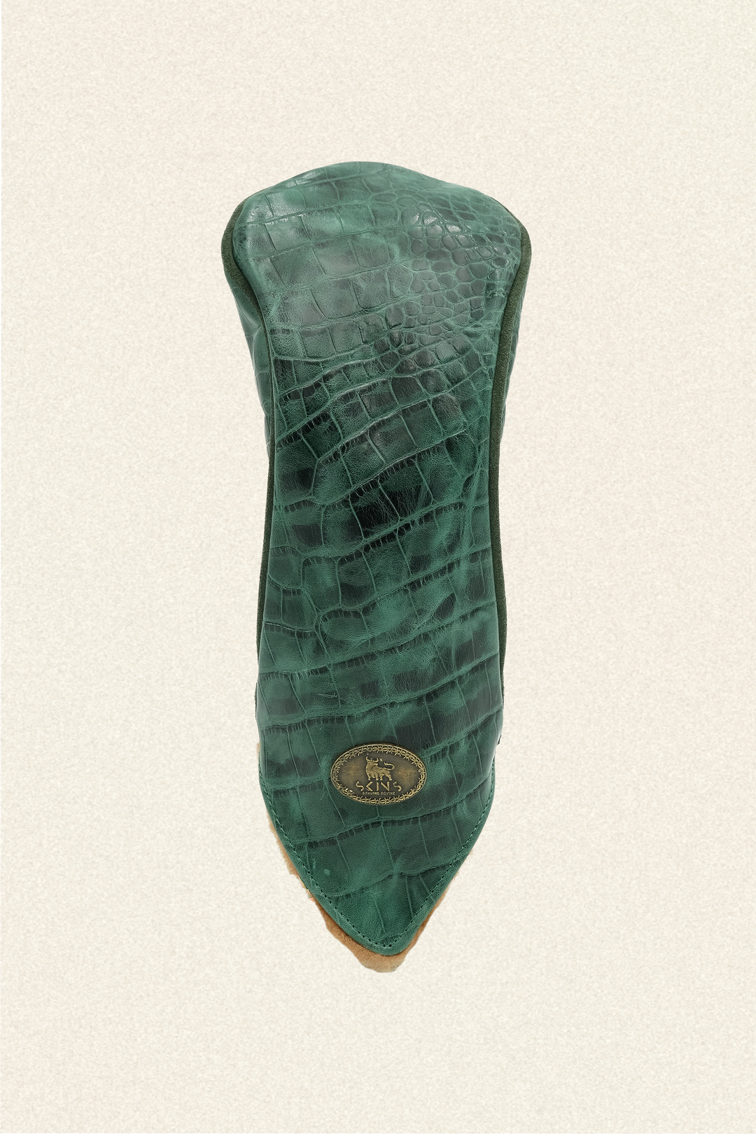 A green crocodile-embossed leather golf club headcover with a gold-tone circular logo badge, shown against a textured off-white background.