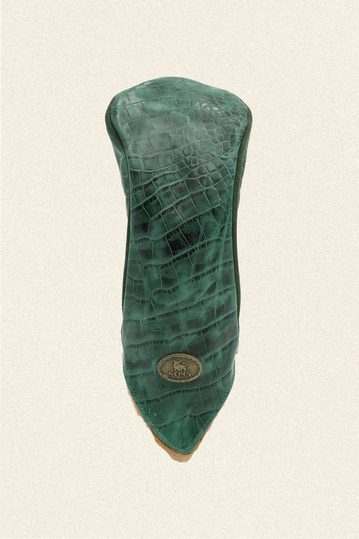 A green crocodile-embossed leather golf club headcover with a gold-tone circular logo badge, shown against a textured off-white background.