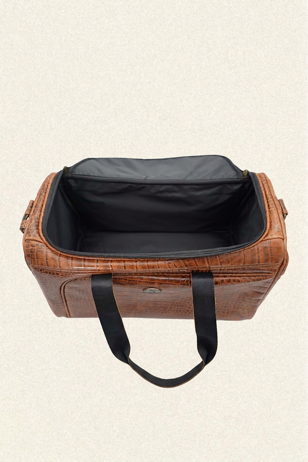 A brown crocodile-embossed leather duffel bag with black handles and a black interior, shown open against a light beige textured background.