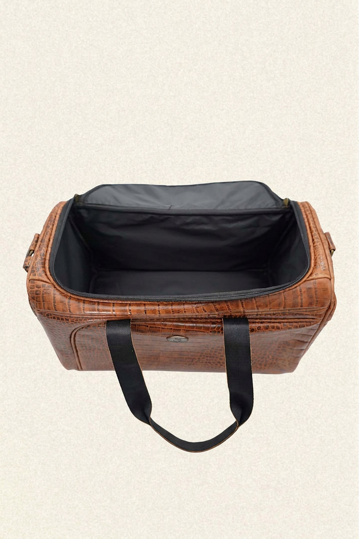 A brown crocodile-embossed leather duffel bag with black handles and a black interior, shown open against a light beige textured background.