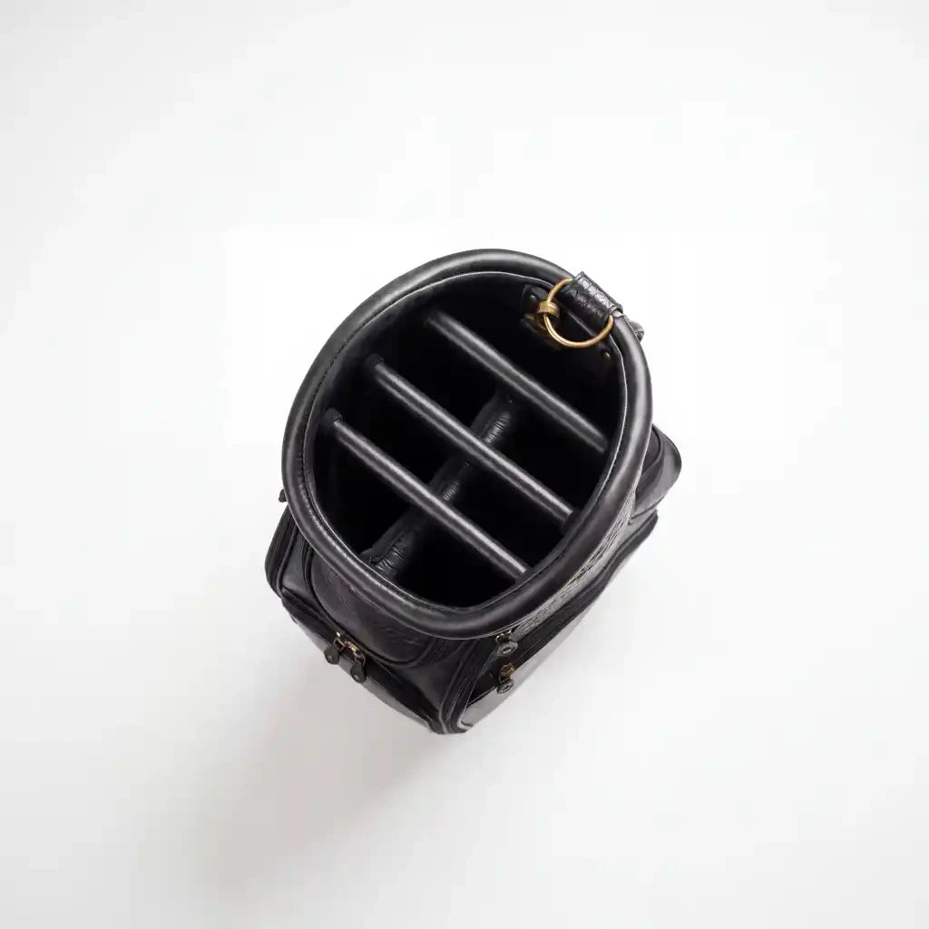 Black leather cylindrical pouch or organizer shown from a top-down view, featuring a structured interior with four vertical dividers and a small gold-tone ring detail, set against a plain white background.