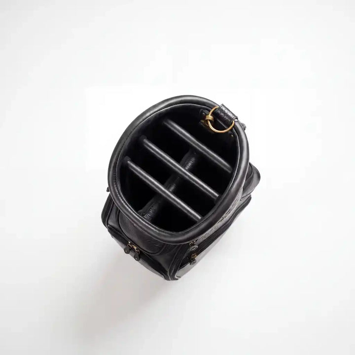 Black leather cylindrical pouch or organizer shown from a top-down view, featuring a structured interior with four vertical dividers and a small gold-tone ring detail, set against a plain white background.