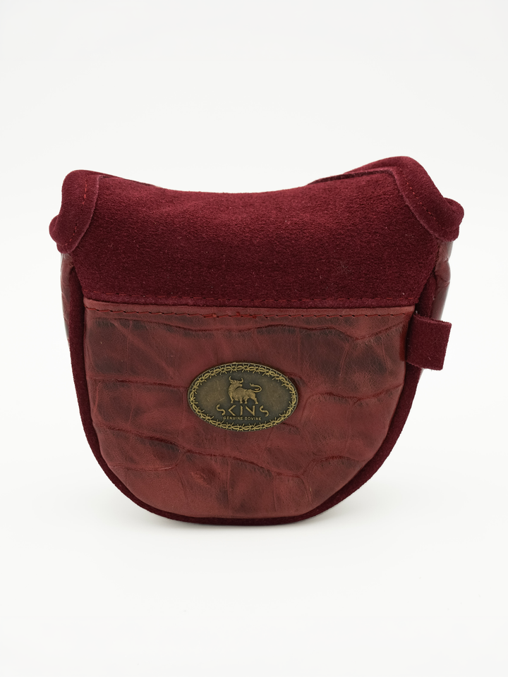 A burgundy split-material pouch with a suede-like top half and a textured faux-croc bottom half, featuring a circular brass and green logo patch on the front.