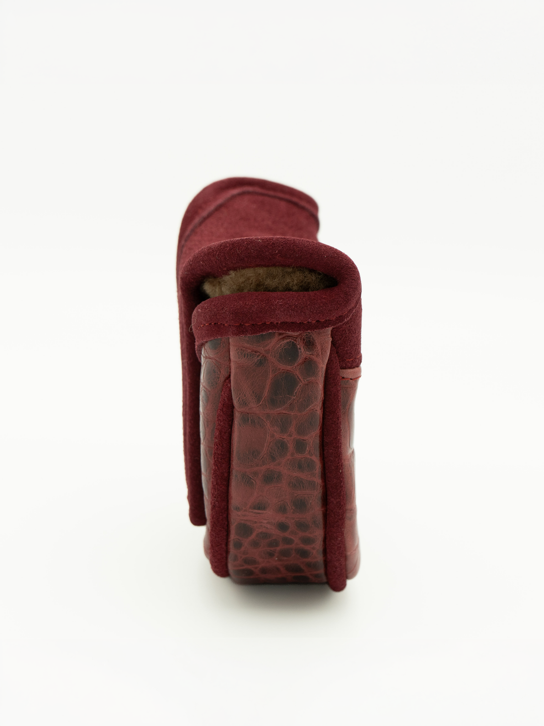A close-up side view of a burgundy leather accessory, showing a textured crocodile-patterned heel or sole section and a soft suede-like upper, set against a plain white background.