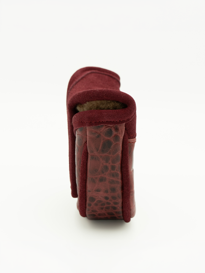 A close-up side view of a burgundy leather accessory, showing a textured crocodile-patterned heel or sole section and a soft suede-like upper, set against a plain white background.