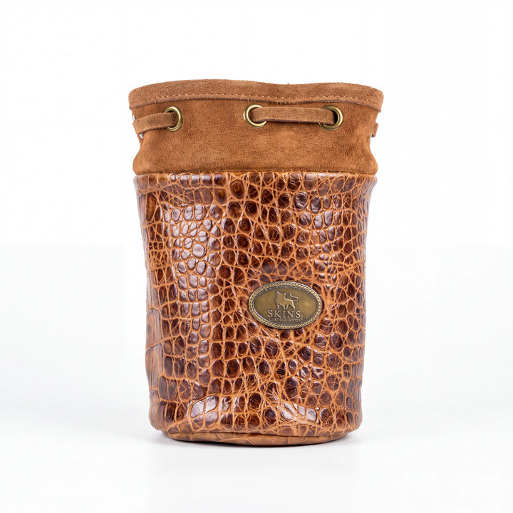 A brown leather pouch with a crocodile-embossed front panel and a suede-like top trim, featuring brass-tone hardware and a round metal logo plaque on the front.